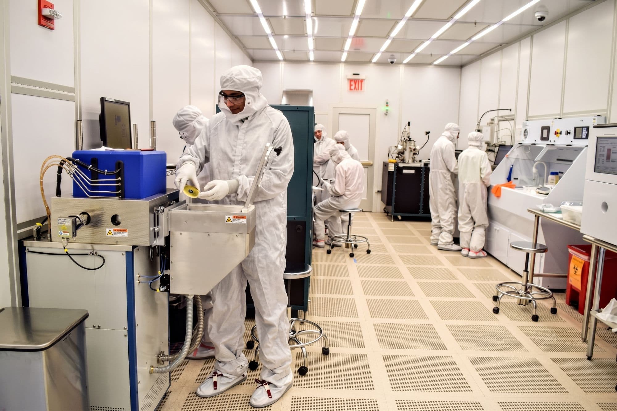 Researchers in cleanroom gowns and hoods working at nanofabrication equipment